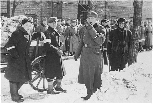 Young Jewish men who have been assigned work clearing snow stand in front of a formation of German troops